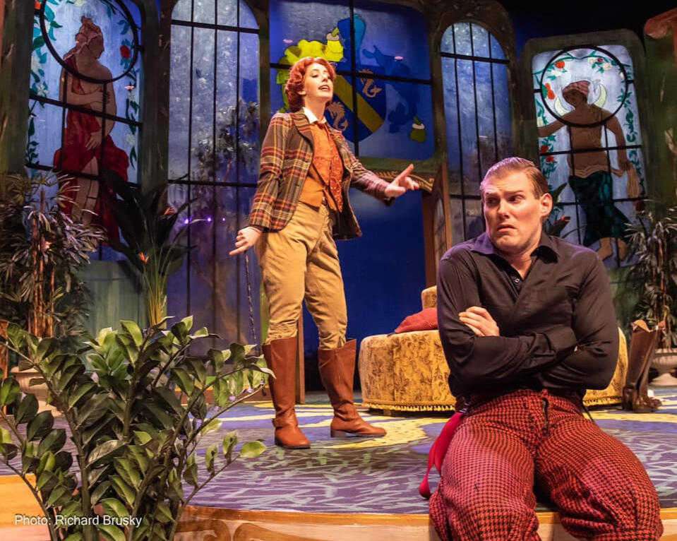A women lecturing a man who sitting on the edge of the stage.