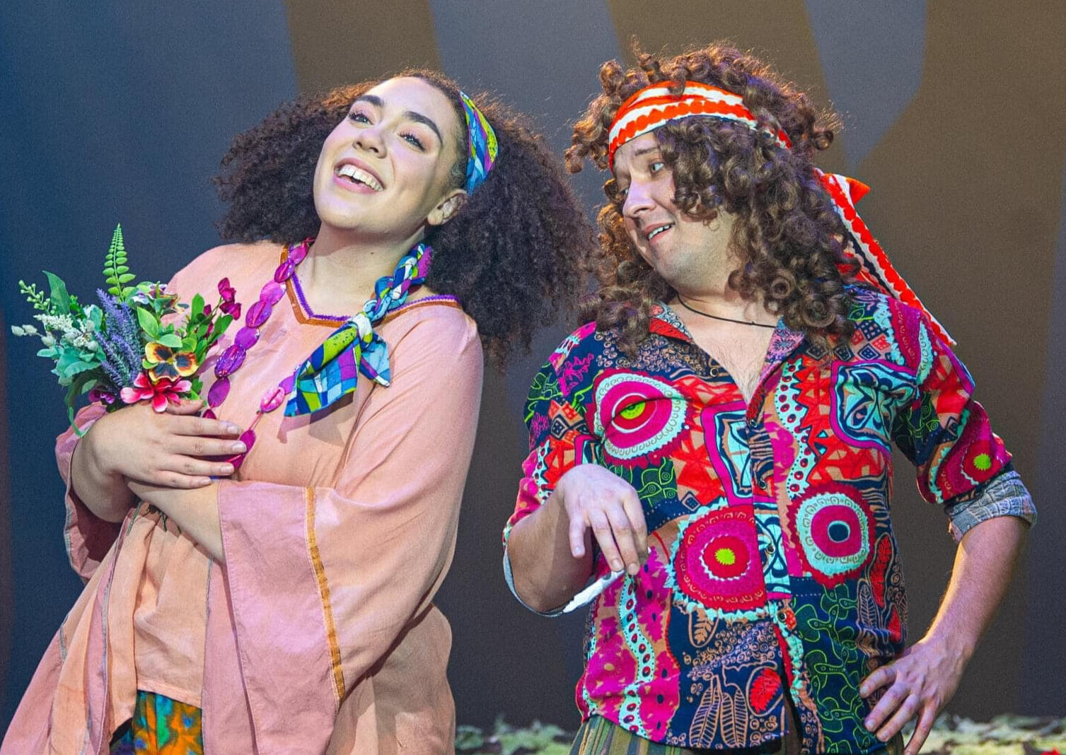 A fairy from A Midsummer Night's Dream and Puck conversating and smiling in 1970's clothing.